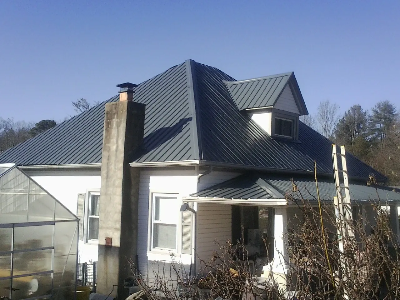 Dark blue standing seam metal roof on a white farmhouse with dormer — Slate & Tile Roof Repair by Roofing Brothers in Clearville