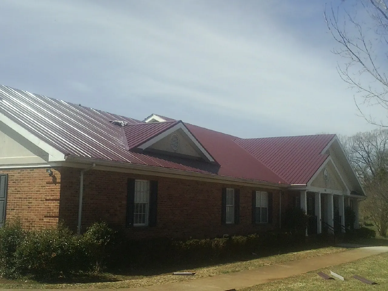 Red metal roof with gabled entries on a long brick building, from a Hail Damage Roof Repair job in Clearville