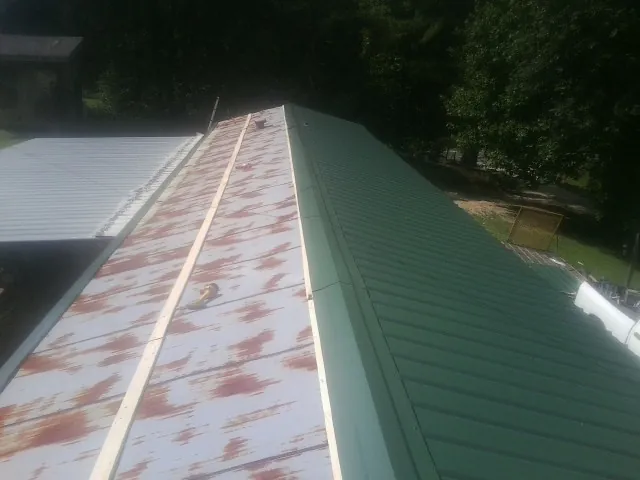 Old rusted panels beside newly installed green metal roofing — Wind Damage Roof Repair by Roofing Brothers in Clearville