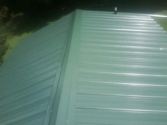 New green metal panels meeting at the ridge of a roof — Flat Roof Repair work by our crew in Clearville