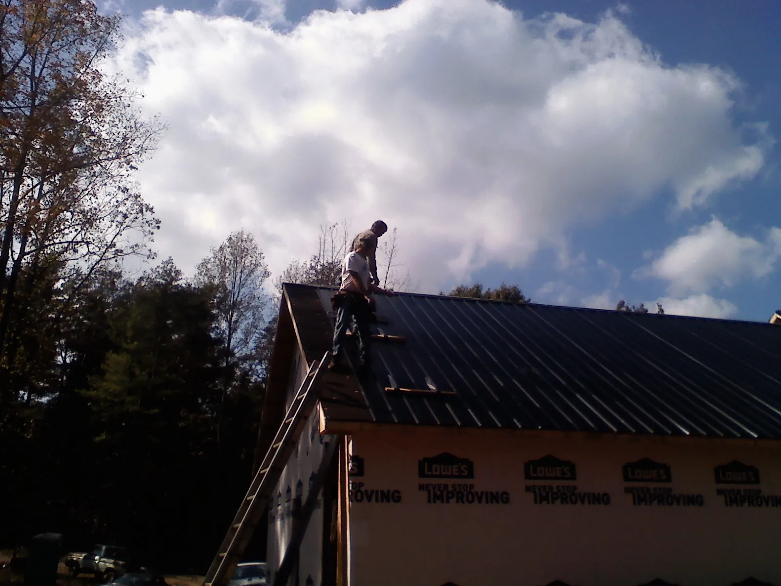 Roofer fastening dark metal panels high against a cloudy sky, from a Roof Inspection job in Clearville