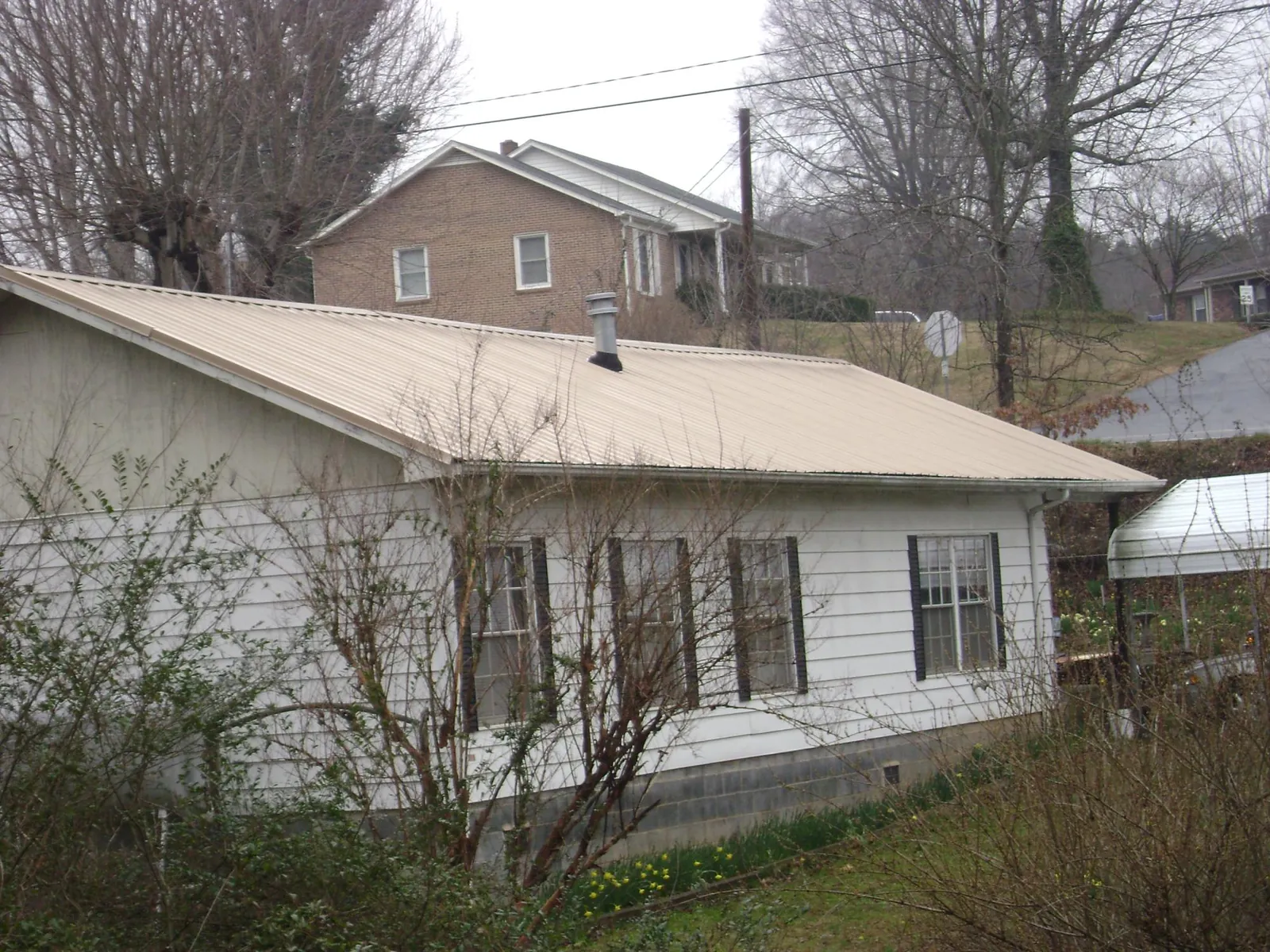 Tan metal roof on a white sided house set into a hillside — Commercial Roofing by Roofing Brothers in Clearville
